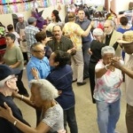 Group shot of several older adult couples dancing. The room is decorated for a party.