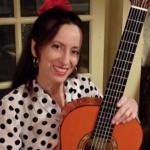 Photo of teaching artist Lisa Spraragen. She has dark hair and has a guitar in her hands. She is smiling.