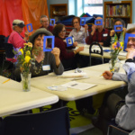 Pictured are participants in a painting workshop at Forest Hills Community Library, Queens. They are posing and smiling.