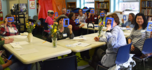 Pictured are participants in a painting workshop at Forest Hills Community Library, Queens. They are posing and smiling. 