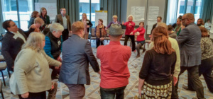 Pictured are participants at a creative aging reconvening in Minnesota. They are huddled in a circle engaged in an exercise.
