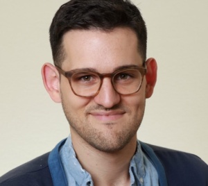 This is a headshot of Lifetime Arts Trainer, Vinny Mraz. He has dark brown hair and brown glasses. He is smiling. 