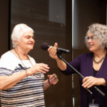Two women stand at a microphone before a storytelling performance.