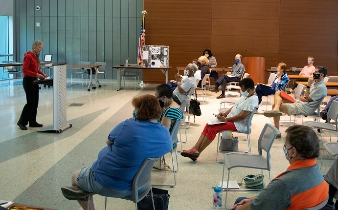 A photo of a participant at a podium presenting to other participants seated in rows.