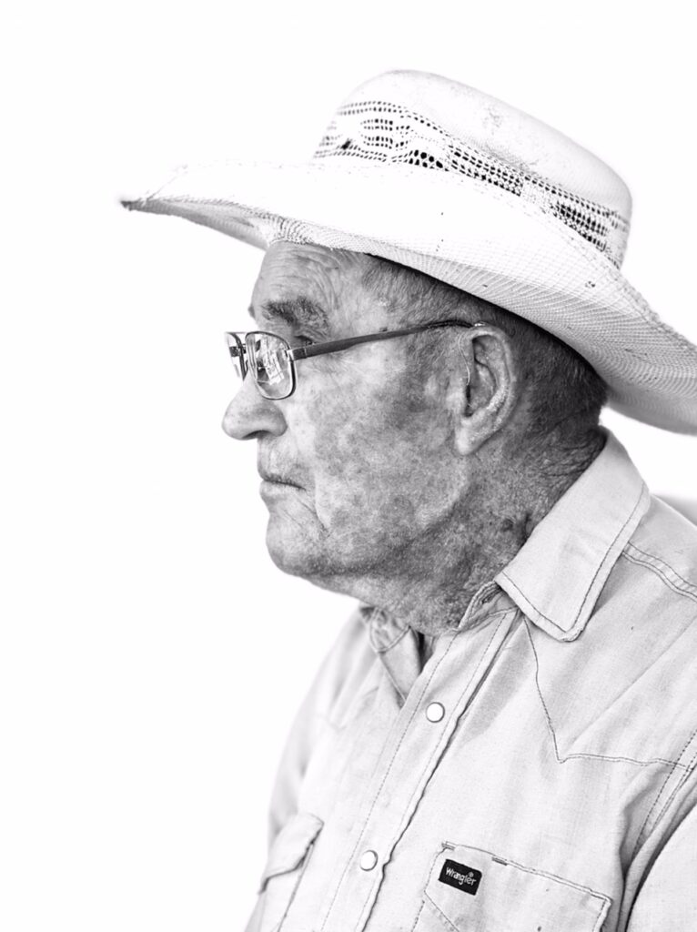 A black and white profile of an older man with glasses and a western hat