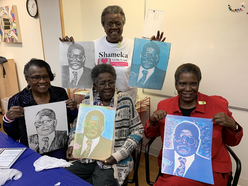 Older adult participants smile and pose with their printmaking projects.