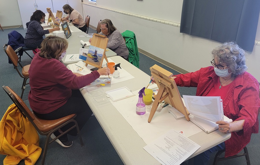 A photo of a group of participants painting at a table on small easels. 